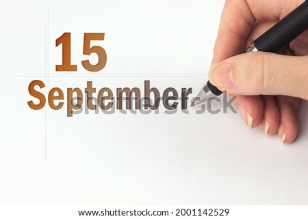 September 15th. Day 15 of month, Calendar date. The hand holds a black pen and writes the calendar date. Autumn month, day of the year concept