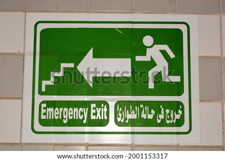 Emergency Fire Exit sign in corridor point way out of the building to escape in case of emergency, urgency and fire, Translated Arabic words ( exit in case of emergency ), man running towards stairs.