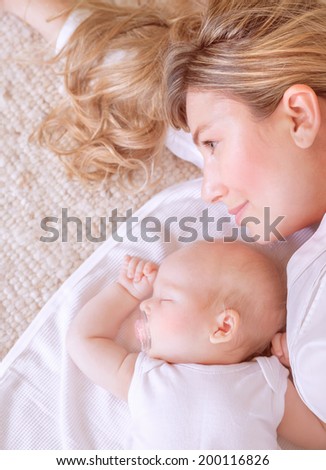Closeup picture of beautiful young mother lying down with her sweet sleeping newborn child, loving family, new life concept