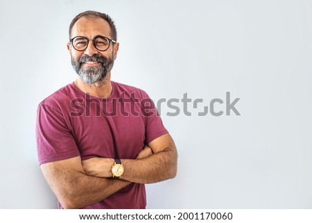 Portrait of happy mature man wearing spectacles and looking at camera indoor. Man with beard and glasses feeling confident.  Handsome mature man posing against a grey background Royalty-Free Stock Photo #2001170060