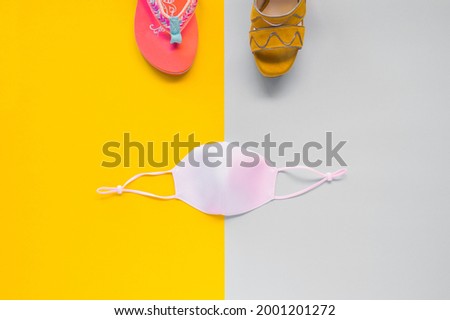 Flip-flops, high-heeled sandals and a mask on a yellow and gray cardboard. Summer and coronavirus concept with different shoes neatly on a background divided in half. Top view, symmetry.