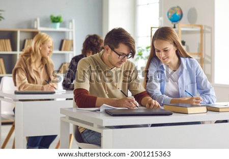 University students studying sitting at desk in classroom. Smart guy explaining girl hard interesting problem. Mutual help, buddy system, mentoring, college peer tutoring, giving useful tips, cheating Royalty-Free Stock Photo #2001215363
