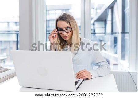 Caucasian happy young freelancer woman sitting at table and talking online on webcam remotely. Female student tells and communicates video call with friends or family indoors. Home or modern office