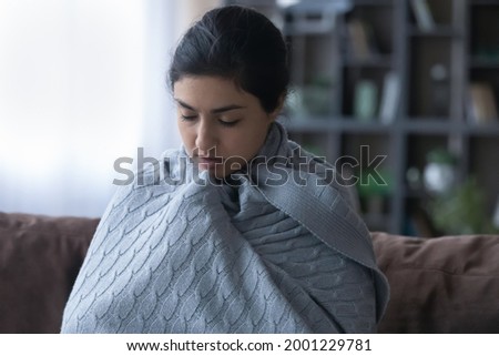 So cold. Young indian woman wrap up in blanket freeze at home feel ague shiver because climate control heating system is broken. Sick female teenager trying to warm up in cool living room under plaid Royalty-Free Stock Photo #2001229781