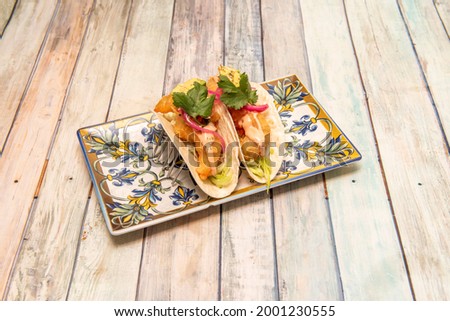 tacos with crunchy tortillas stuffed with seafood battered with iceberg lettuce and parsley on wooden table