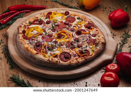 Whole rustic Pizza with salami, hunting sausage, jalapeno pepper, onion Rings served on wooden plate