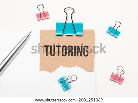 Business and finance concept. On a white background lies a notebook, a pen, clothespins and cardboard with the inscription - TUTORING