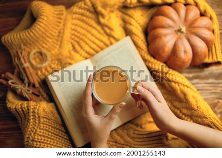 Vintage book with romantic stories and fairy tales. Top view of autumn composition with book and knitted sweater. Hot cocoa in hands, ripe pumpkin, warm sweater and open book on wooden background.  Royalty-Free Stock Photo #2001255143