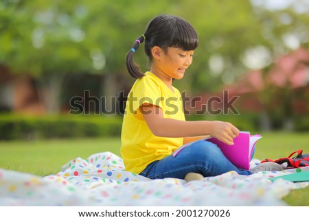 Cute little girl  reading books on the grass. She has a look of enjoyment of life on her face and she looks very relaxed. Which increases the development and enhances learning skills outside the room.