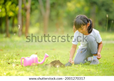 Cute little girl asia planting young tree on black soil in the park.Which increases the development and enhances learning skills as save world new life,environmental conservation concept.