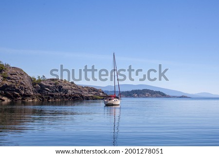 A sailboat is anchored (moored) in a small cove on the southern end of Thormanby Island, on the Sunshine Coast. A popular spot for summer cruising.