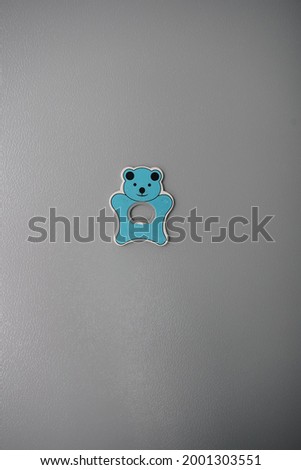 A blue bear shape magnet bottle opener on gray refrigerator wall for grey background