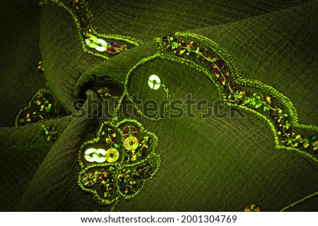 Silk green. The fabric is embellished with sequins. background, silk satin, luxurious texture, dark fabric, costume cotton material, abstract color image pattern, delicate liquid emerald velvet