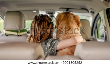 Preteen girl hugging golden retriever dog and sitting in the car inside. Child kid with purebred doggy pet in the vehicle from the back Royalty-Free Stock Photo #2001305252