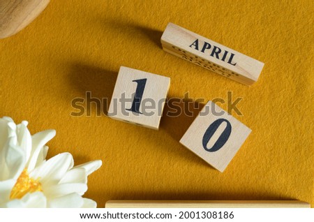 April 10, Wooden Calendar cube on yellow felt fabric with peony flower for date icon background.