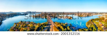 Turns of Parramatta river in Inner west of Sydney under Gladesville bridge. Aerial panorama towards city CBD skyline. Royalty-Free Stock Photo #2001312116
