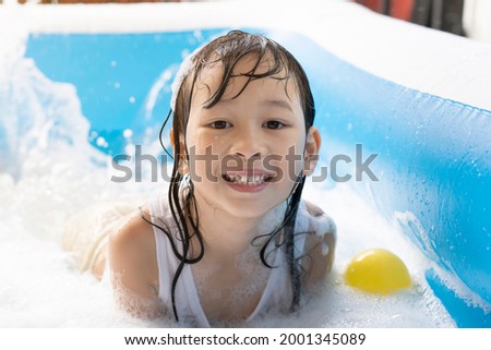 Beautiful Asian girl playing in an inflatable pool. Playing in the water at home during the summer. bubble play, family happiness, children playing in the water