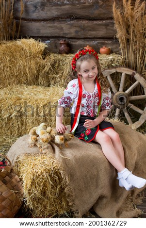 Girl in a Ukrainian folk costume plays with chickens in bales of straw. Happy Easter