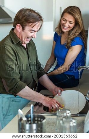 Man washing the dishes with his wife next to him.