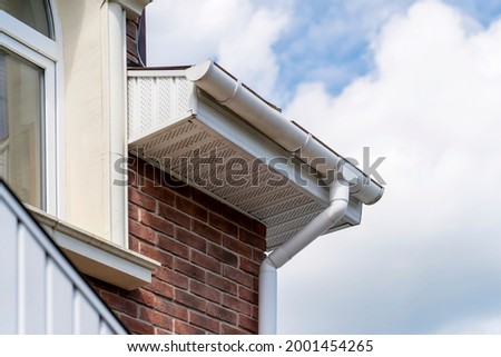 Closeup view of old white gutter system with soffit vent, gutter guard, downspout, decorative trim molding, on corner of brick luxury house