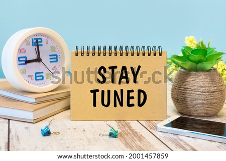 A sign with the inscription Stay Tuned on the table with office supplies
