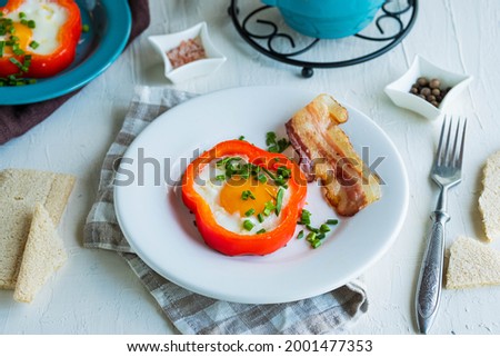 Breakfast, fried egg in red sweet pepper with bacon on a white ceramic plate on a light concrete background. Egg recipes.