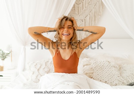 Woman stretching in bed waking up in cozy bedroom with bohemian interior style. Female wearing in comfort pajamas enjoying early morning,.
