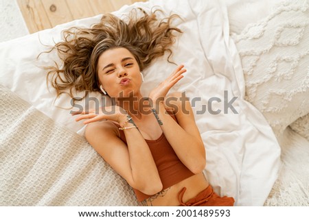 Playful girl having fun and making grimaces while chilling in her bed. Top view. Cozy home. Lying on back. 
