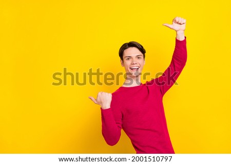 Photo of impressed funny young gentleman wear red pullover pointing thumbs up empty space smiling isolated yellow color background