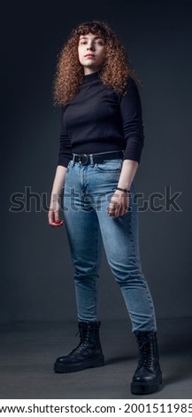 Full length portrait of young woman heroic posing with curly hair on gray background. Studio shoot, fashion concept.