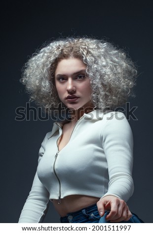 Portrait of serious young woman with curly white hair on gray background. Studio shoot, fashion concept.