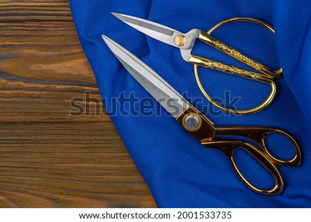 Cut and sew customized garments, sewing accessories. Scissors, blue fabrics on a wooden table.