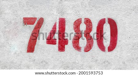 Red Number 7480 on the white wall. Spray paint. Number seven thousand four hundred and eighty.