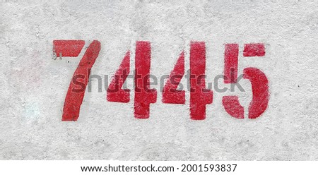 Red Number 7445 on the white wall. Spray paint. Number seven thousand four hundred forty five.