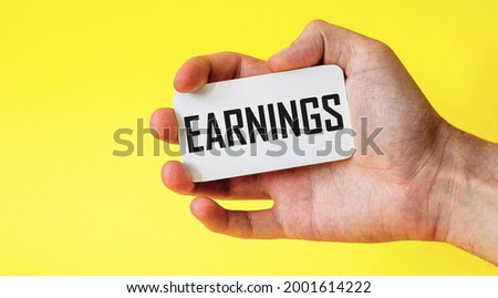 Hand holds a card with the word earnings on a yellow background