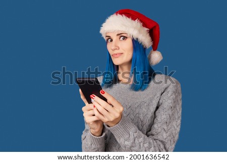 Beautiful happy young woman in santa hat with smartphone over blue background