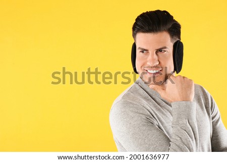 Man wearing stylish earmuffs on yellow background. Space for text