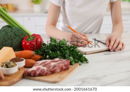 Woman with notebook and healthy food at white table, closeup. Keto diet Royalty-Free Stock Photo #2001661670