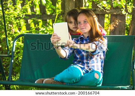Young sisters shoot selfie on a tablet PC in the park.