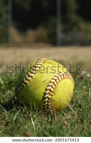 Yellow softball with red seams outside on green grass.