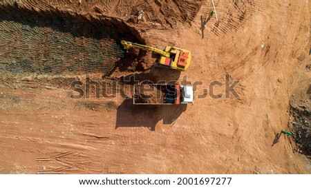 Aerial photo of excavator pours sand into the truck. On construction site top view. Drone shooting. Earthmoving equipment.