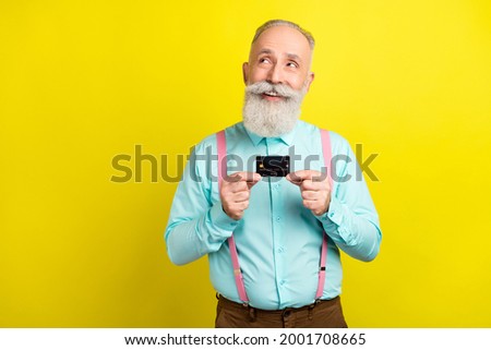 Photo of cunning old man hold card look empty space wear blue shirt isolated on yellow color background
