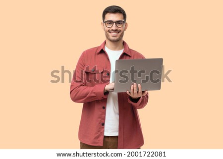Young man standing holding laptop and looking at camera with happy smile