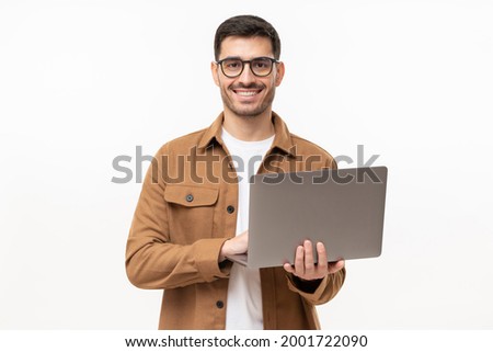 Studio portrait of young man standing holding laptop and looking at camera with happy smile, isolated on gray