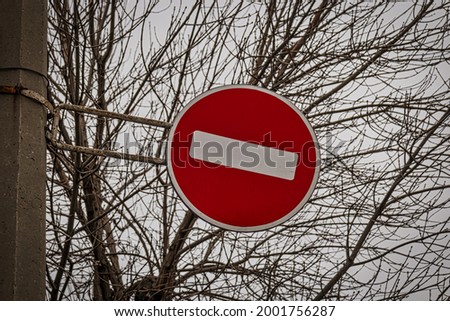 Brohibiting road sign brick set against bare tree branches as a symbol of restrictions in human life