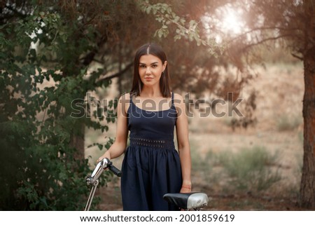 a young brunette woman of Asian appearance in a dark blue dress is standing next to a bicycle with a punctured wheel. there is a grain and a small depth of focus in the photo for artistic purposes.