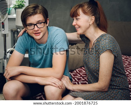 Photo of family relationships. Mom hugs her son at home while sitting on the sofa with a smile