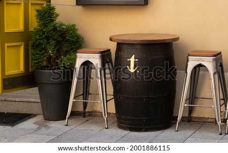 Barrel table and metal stools on the street near the cafe. Royalty-Free Stock Photo #2001886115
