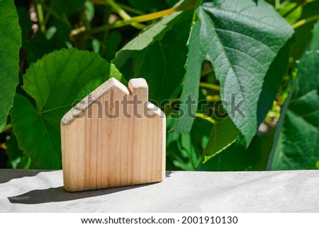 Wooden toy house symbol on light surface against background of green foliage of vine with copy space. The concept of buying country house for growing grapes, peace, quiet in private house in nature.