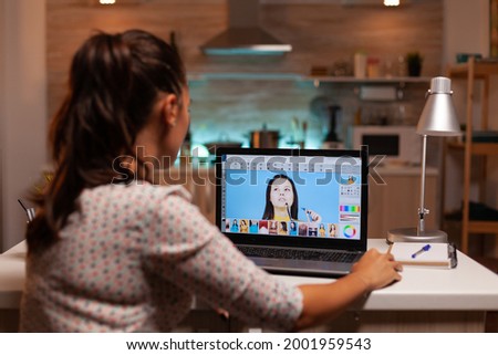 Professional graphic editor retouching photos of a client during night time in home office. Photographer doing portrait post production using software and performance laptop, artist, occupation